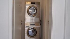 A compact, stainless steel, wall-mounted washer and dryer unit with a control panel and a small storage compartment.