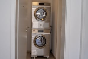 Un appareil compact, en acier inoxydable, comprenant une laveuse et une sécheuse à installer au mur, doté d’un panneau de commande et d’un petit compartiment de rangement.
