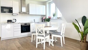 A modern kitchen with white cabinetry, a built-in oven, and a dining area with white chairs and a table.