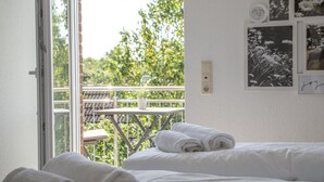 A bedroom with a large window, a balcony, and a bed with rolled towels.