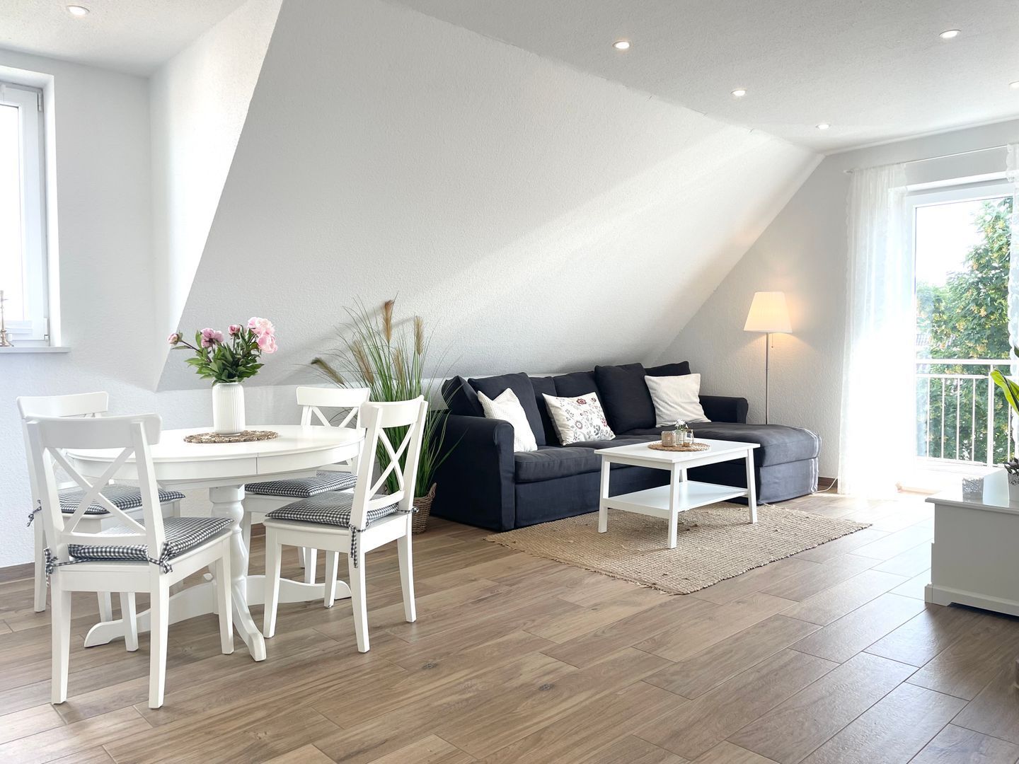 Un salon moderne comprenant un coin repas, un canapé foncé, des chaises blanches et une petite table.