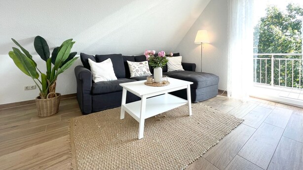 Ein modernes Wohnzimmer mit einer Couch, einem Couchtisch, einer Lampe und einer Pflanze.