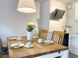 Une cuisine moderne avec des armoires blanches, un four encastré et un coin repas comprenant une table et des chaises en bois.