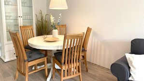 A dining area with a round table, six wooden chairs, a vase with flowers, and a hanging lamp.