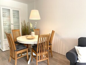 A dining area with a round table, six wooden chairs, a vase with flowers, and a hanging lamp.