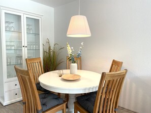 A round dining table with wooden chairs, a white cabinet with glass doors, and a hanging lamp.