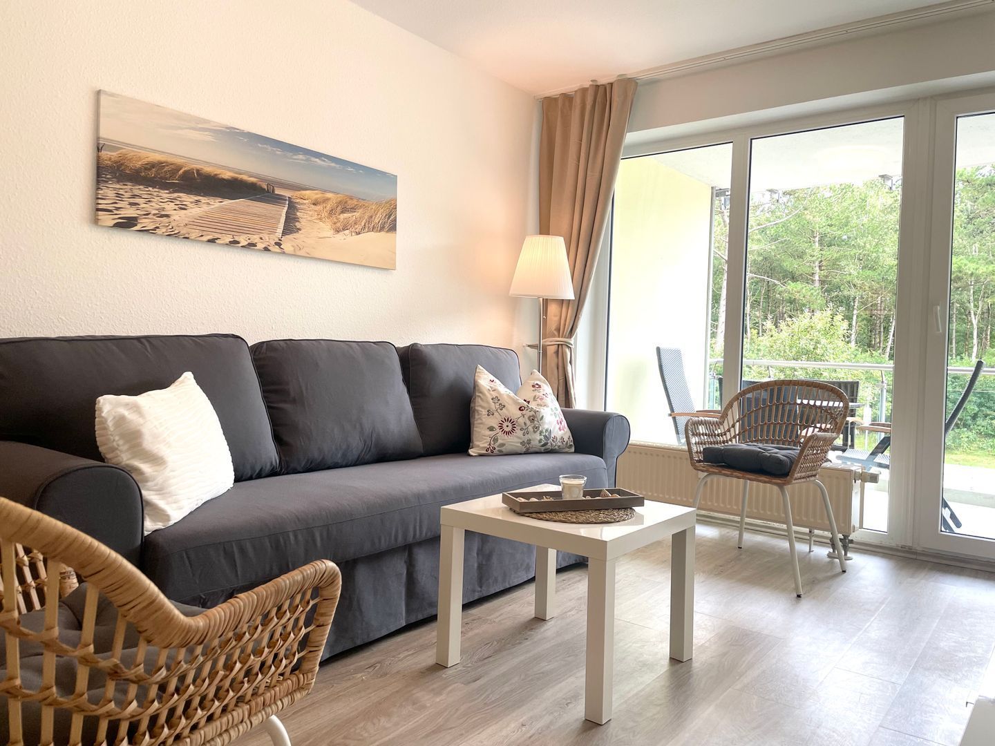 Een woonkamer met een bank, een salontafel, rieten stoelen, een schilderij aan de muur en uitzicht door grote ramen.