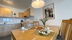 A modern kitchen with wooden cabinets, a dining table with plates of food, and a vase of flowers. - A1.4 - Exclusive vacation apartment with balcony, close to the beach for up to 7 people - (Cuxhaven)