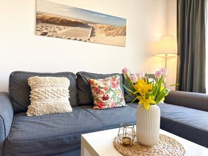 A living room with a grey sofa, decorative pillows, a vase with flowers, a lamp, and a painting on the wall. - A1.4 - Exclusive vacation apartment with balcony, close to the beach for up to 7 people - (Cuxhaven)