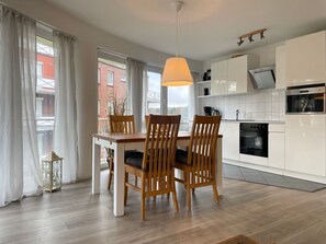 Una cocina moderna con armarios blancos, horno empotrado y una zona de comedor con mesa y sillas de madera.