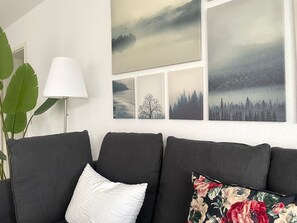 Ein Wohnzimmer mit einem grauen Sofa, einer weißen Lampe und einer Wand mit vier gerahmten Bildern.