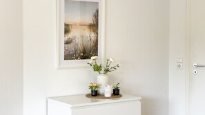 Una puerta blanca con un cuadro enmarcado encima, una consola blanca con un florero y un timbre.