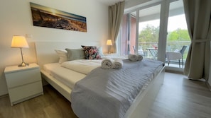A hotel room with a bed, two bedside lamps, a painting on the wall, and a balcony with a table and chairs.