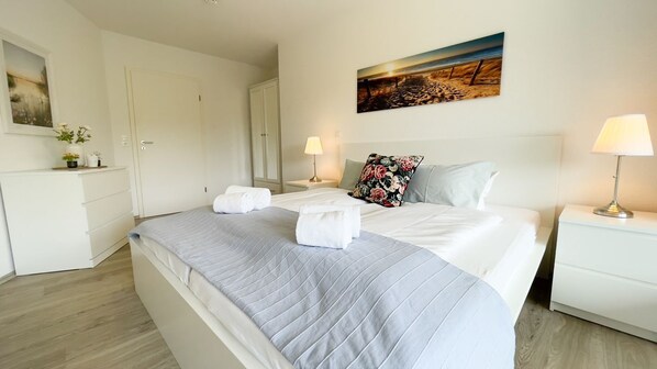 Un cuarto de hotel con una cama grande, una mesita de noche con lámpara, un cuadro en la pared y un armario.