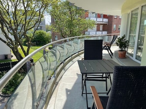 A balcony with a glass balustrade, a table, two chairs, and a potted plant.