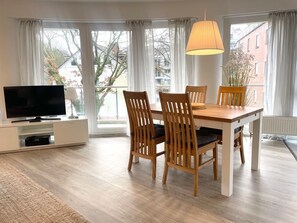 Una sala de estar moderna con televisor de pantalla plana, mesa de comedor de madera y sillas.