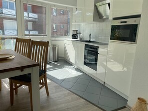 Una cocina moderna con armarios blancos, horno empotrado y ventana con vistas a un edificio de ladrillo.