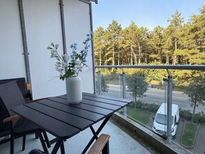 A balcony with a table and chairs, a vase with flowers, and a view of a road with a white van.