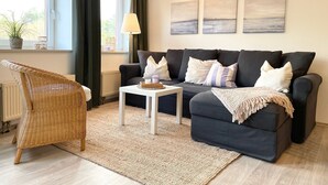 Una sala de estar con un sofá, una silla de mimbre, una mesita y un radiador.