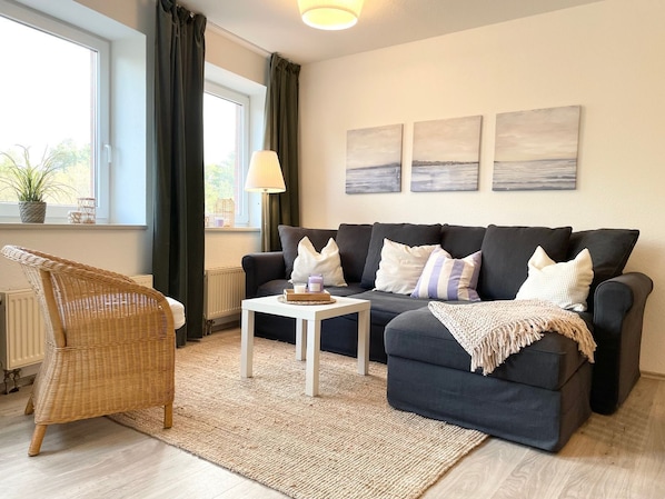 Una sala de estar con un sofá, una silla de mimbre, una mesita y un radiador.