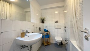 A bathroom with a white sink, toilet, and bathtub, a mirror, and a shelf with toiletries.