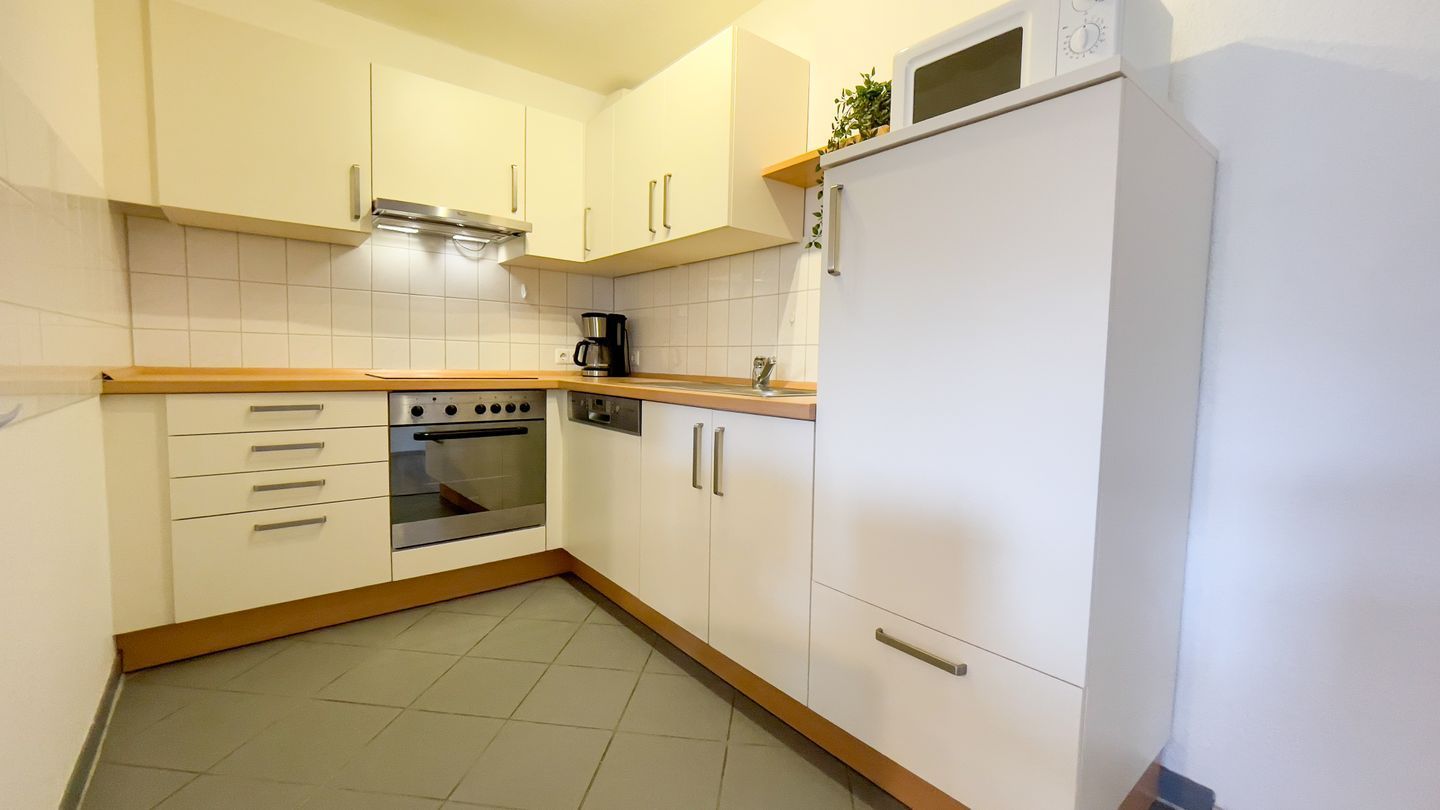 A kitchen with white cabinets, a built-in oven, a microwave, and a coffee maker.