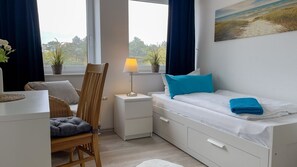 Un dormitorio con cama, una silla, una mesita de noche, una lámpara y una ventana con vistas.