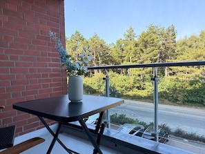 A balcony with a table and a vase of flowers, overlooking a road and trees.