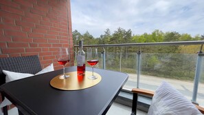 Un balcon avec une table, deux verres de vin rouge et une bouteille de vin.
