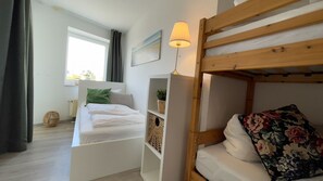 Een stapelbed met een bloemenkussen, een bedlampje en een raam met gordijnen.