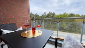 A balcony with a table, two glasses of red wine, and a bottle of wine.