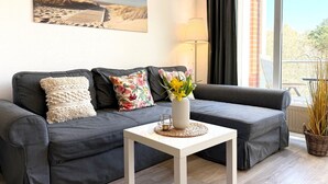 Una sala de estar moderna con un sofá gris, una mesa de centro blanca y un cuadro con motivos playeros en la pared.