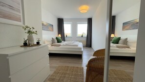 Een moderne hotelkamer met twee bedden, een witte kaptafel, een rieten stoel en kunstwerken aan de muur.