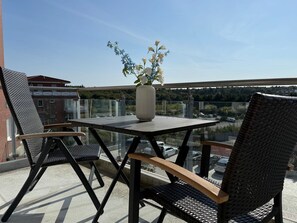 A balcony with a table and two chairs, a vase with flowers, and a view of a parking area and buildings. - A3.1 - Modern, cozy vacation apartment, close to the beach for up to 6 people - House (Cuxhaven)
