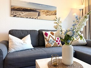 A living room with a grey sofa, decorative pillows, a vase with flowers, a framed picture on the wall, and a lamp. - A3.1 - Modern and cozy apartment near the beach for 6 people - House (Cuxhaven)