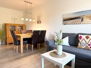 Una sala moderna con comedor, un sofá gris, una mesa de centro blanca y un cuadro en la pared.