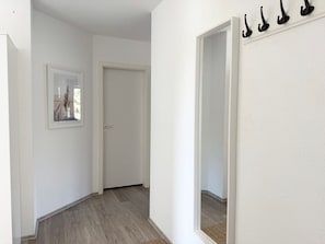 Un pasillo con una puerta, un cuadro enmarco y un espejo con ganchos.