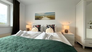 Ein ordentlich bezogenes Bett mit einer grünen Steude, zwei Kissen und einem Wandbild mit Strandmotiv.
