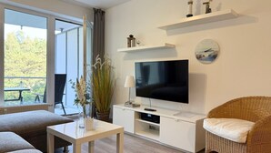 Ein modernes Wohnzimmer mit einem Flachbildfernseher, einem Korbstuhl, einem weißen Couchtisch und einem großen Fenster.