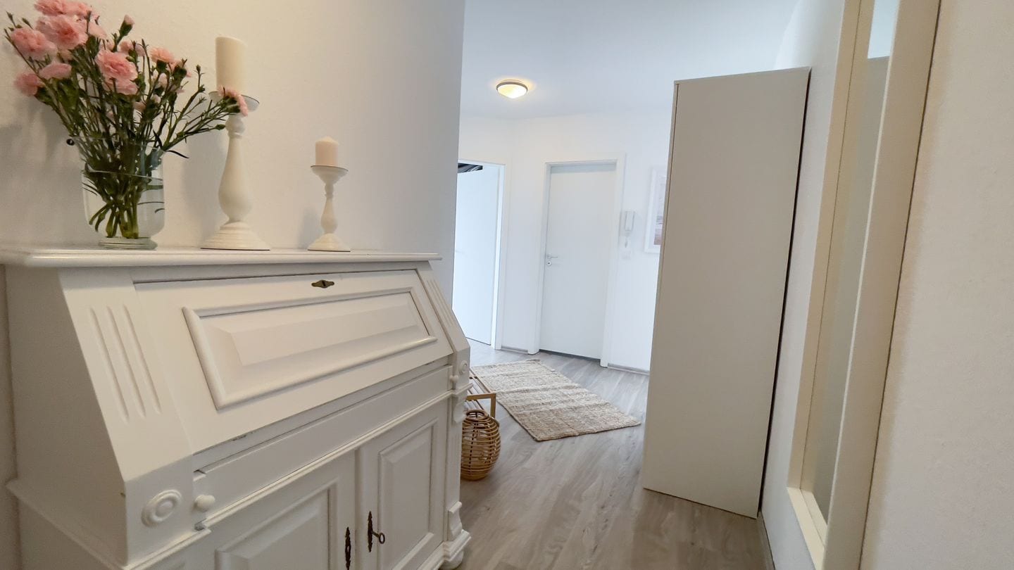 A hallway with a white cabinet, a vase of flowers, and a candle on a shelf.