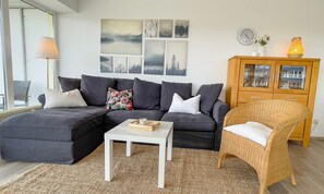 A living room with a sectional sofa, a white coffee table, a wicker chair, and a wooden cabinet with glass doors.