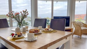 A dining table with food and drinks, a vase of flowers, and a TV in a room with large windows.