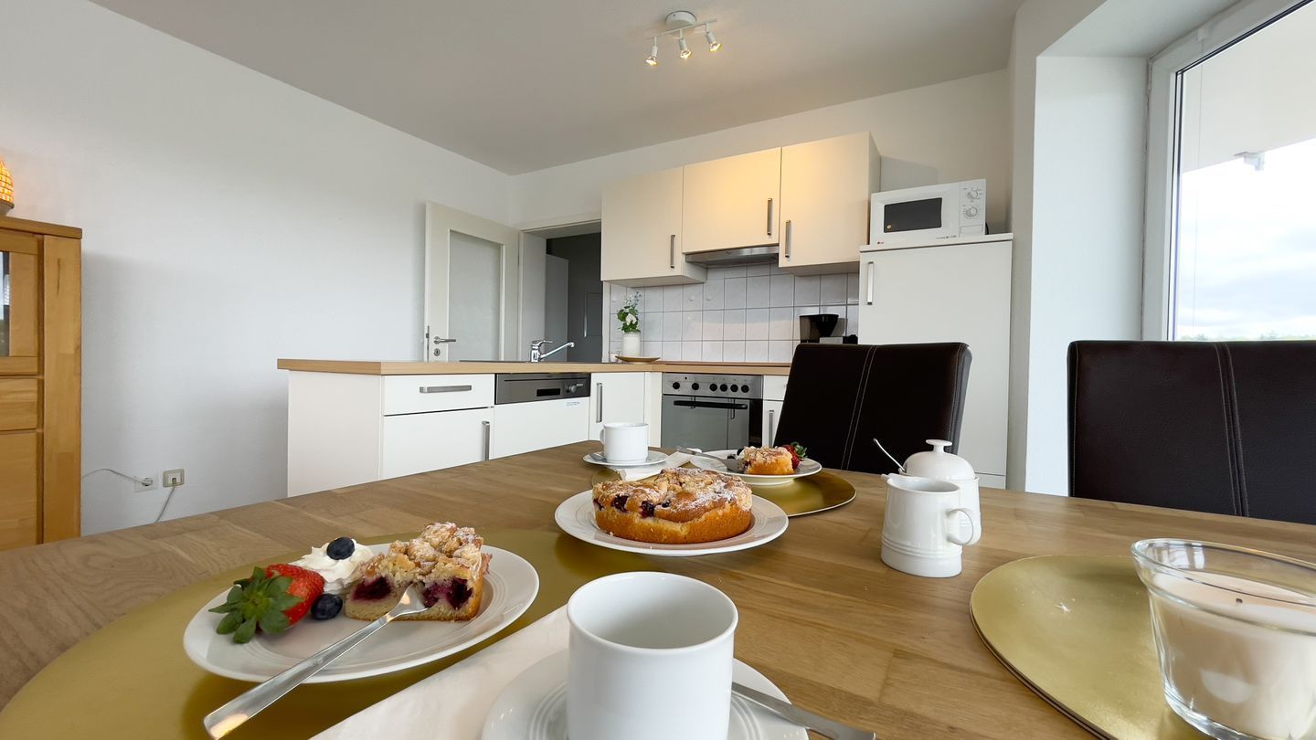 A modern kitchen with white appliances, a dining table with plates of food, and a view through the window.