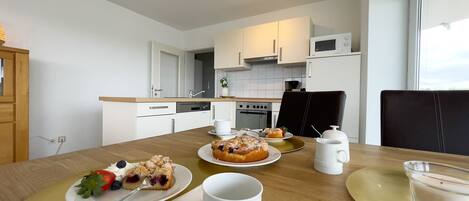 A modern kitchen with white appliances, a dining table with plates of food, and a view through the window.