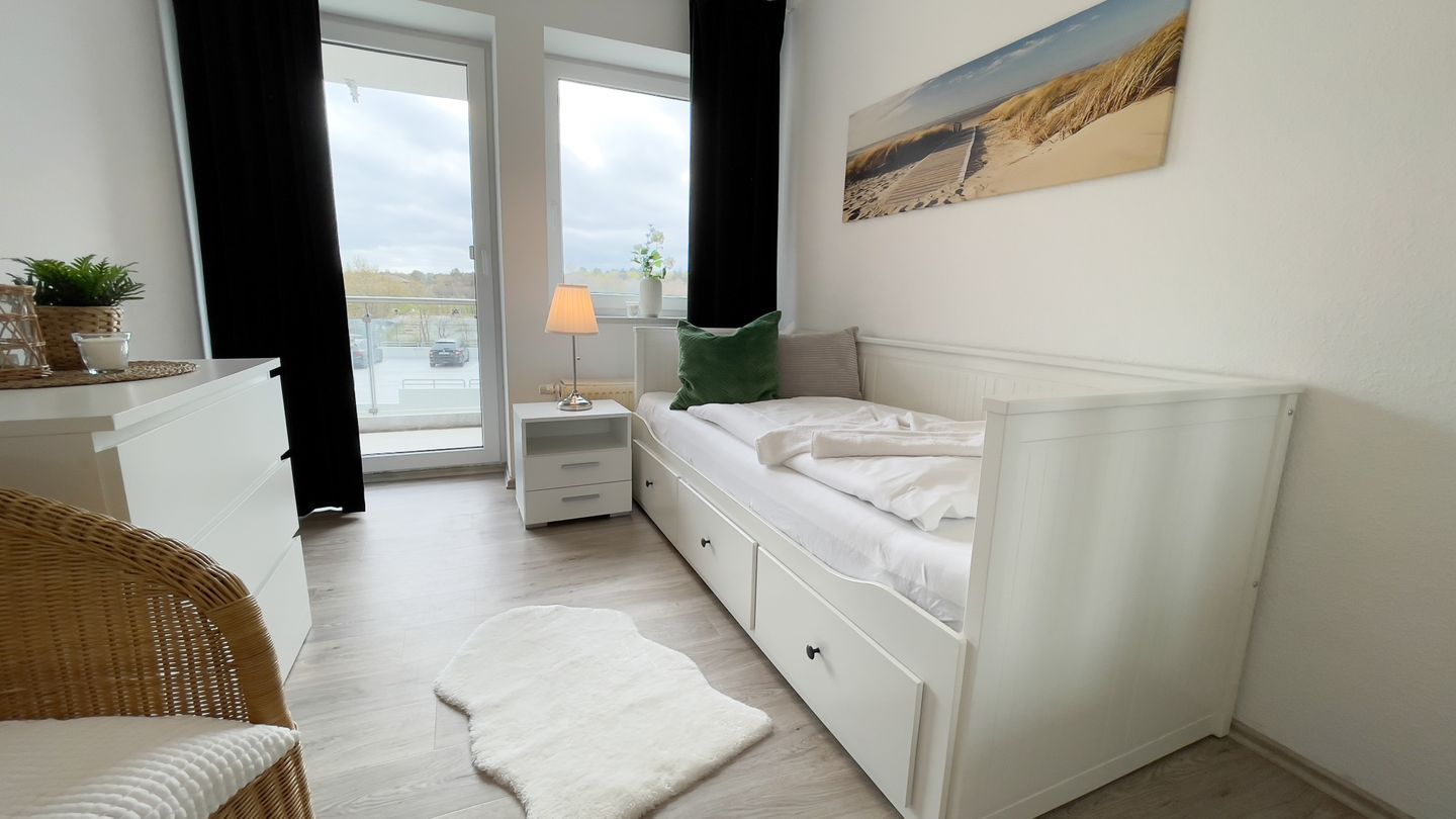 Quarto com cama, mesa de cabeceira, abajur e vista para o exterior.