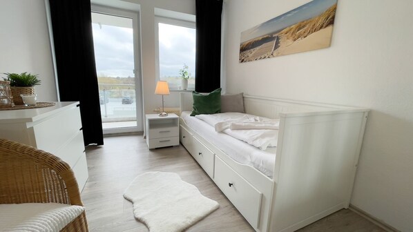 A bedroom with a bed, bedside table, lamp, and a view of the outdoors.