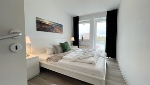 A bedroom with a bed, a nightstand, a lamp, a painting, and a window with curtains.