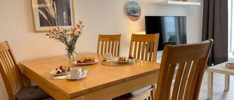A dining area with a wooden table, chairs, a vase of flowers, and a clock on the wall.