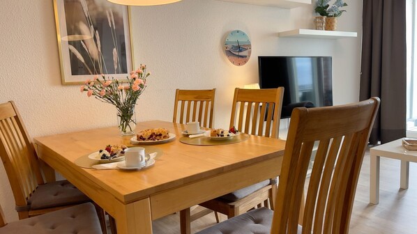 A dining area with a wooden table, chairs, a vase of flowers, and a clock on the wall.