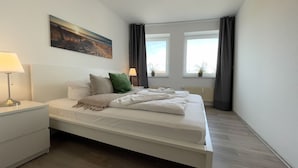 Une chambre à coucher avec un lit, des tables de chevet, un tableau, des fenêtres et des rideaux.